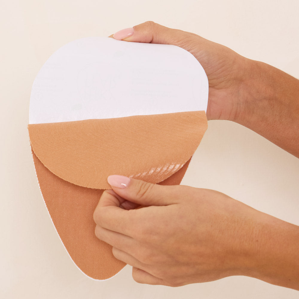 Person applying a adhesive patch on their arm with a plain background
