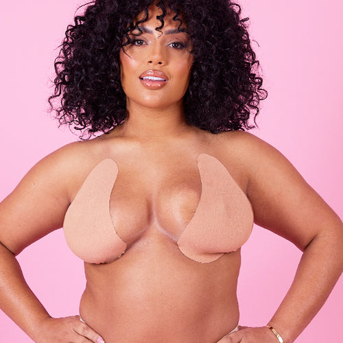 lady with 2 boobs held up by boob tape - perky cleavage, lady has hands on hips with pink background