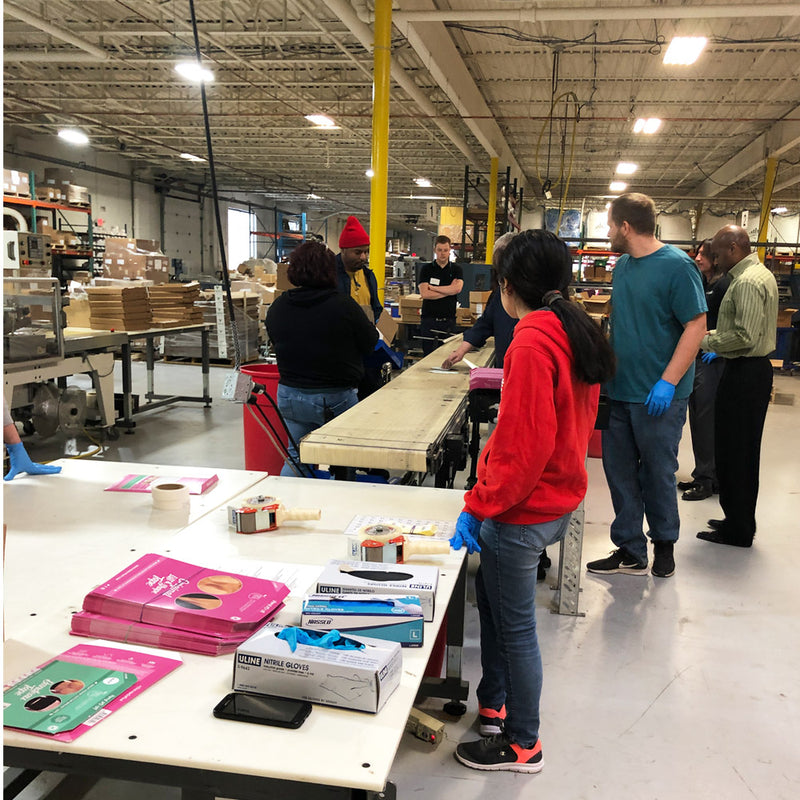 Group of people in a warehouse setting, likely involved in a quality control or inspection process.